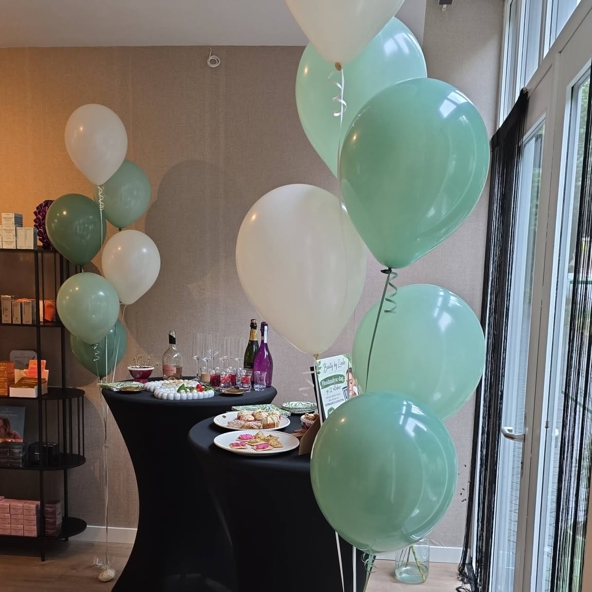 De hoek van de salon met groene en crèmekleurige ballonnen en een productkast